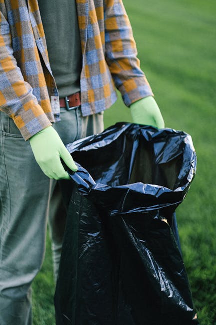 A large pile of black garbage bags stacked against a building wall made of beige tiles, with some plastic bottles and miscellaneous waste visibly protruding from the bags. The bags are crumpled and ti